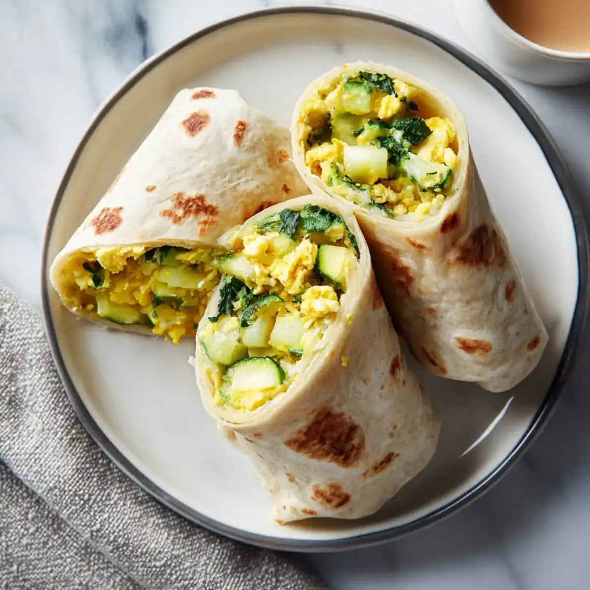 Three cut freezer breakfast burritos recipe on a plate, filled with eggs, zucchini, and greens.
