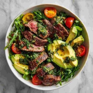 30 Minute Steak Salad; Tender seared steak slices, creamy avocado, and juicy cherry tomatoes tossed with vibrant greens and topped with a zesty chimichurri dressing.