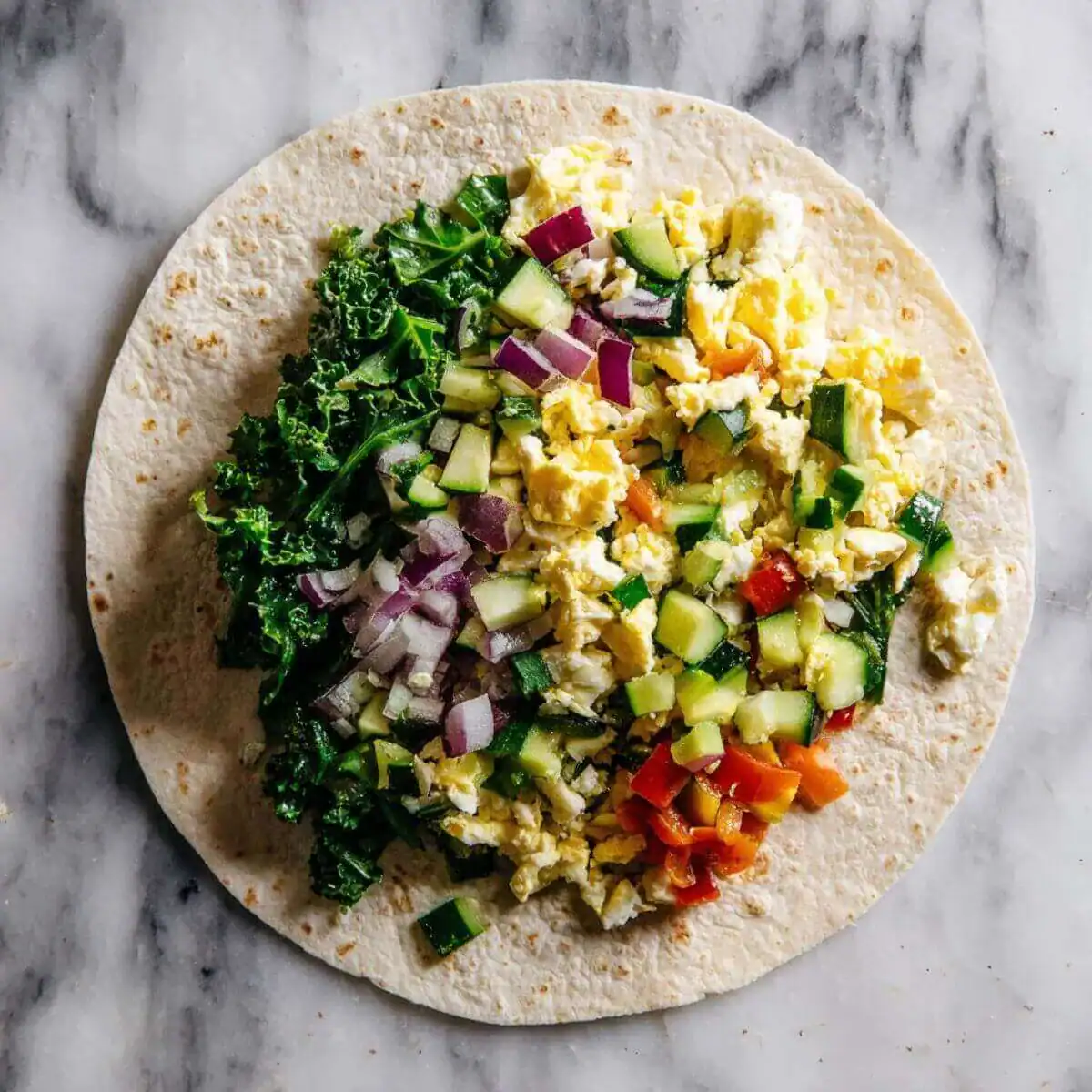 Open tortilla filled with scrambled eggs, kale, chopped zucchini, red onion, and diced red bell peppers.