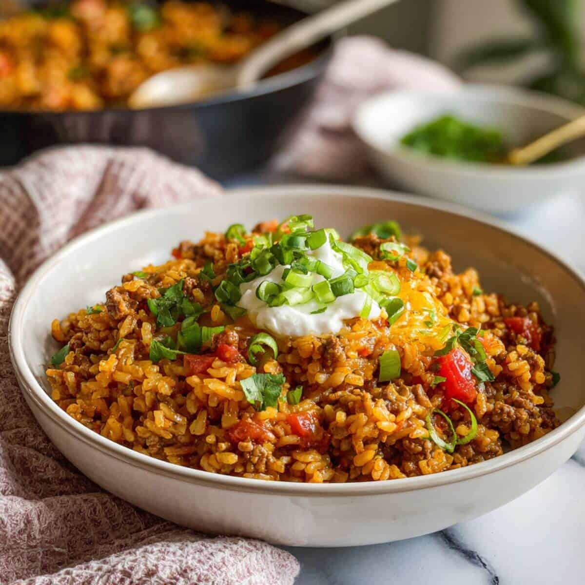 One-pot taco rice topped with sour cream, shredded cheese, green onions, and fresh cilantro in a white bowl.