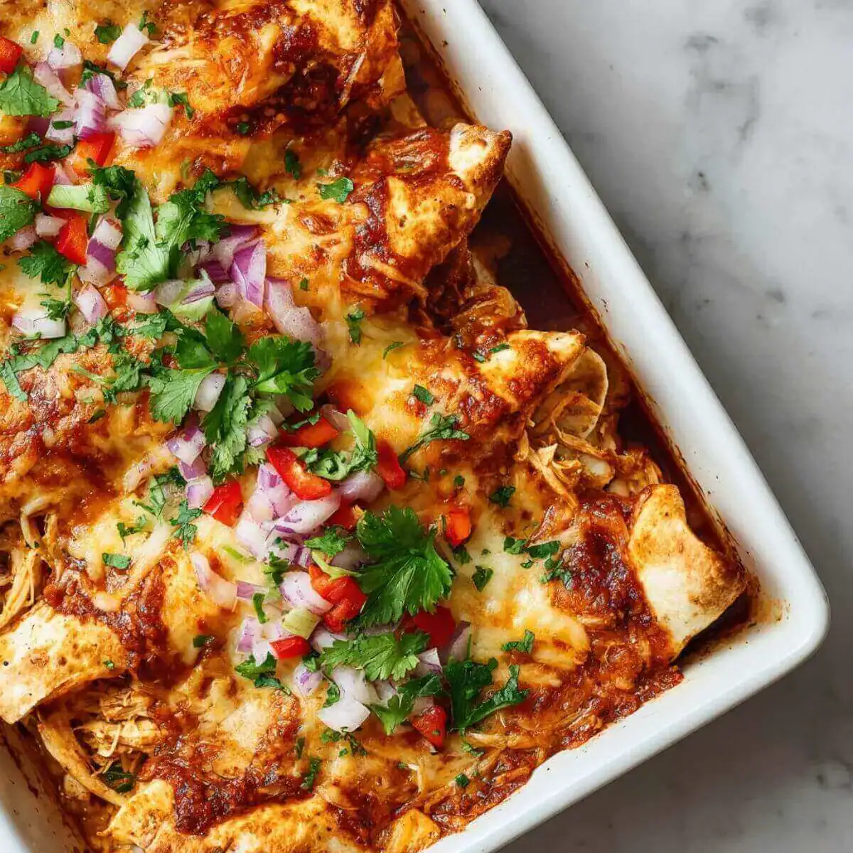 Freezer Chicken Enchiladas Recipe in a baking dish topped with melted cheese, red onion, diced red peppers, and fresh cilantro.
