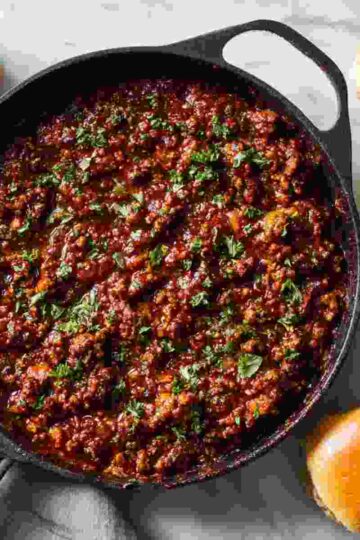 Overhead shot of Freezer Sloppy Joes in a skillet, with rich, glossy sauce coating the ground beef and soft hamburger buns on the side.