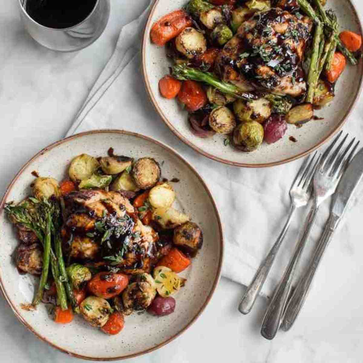 Plated balsamic chicken with roasted vegetables including Brussels sprouts, carrots, asparagus, and potatoes.
