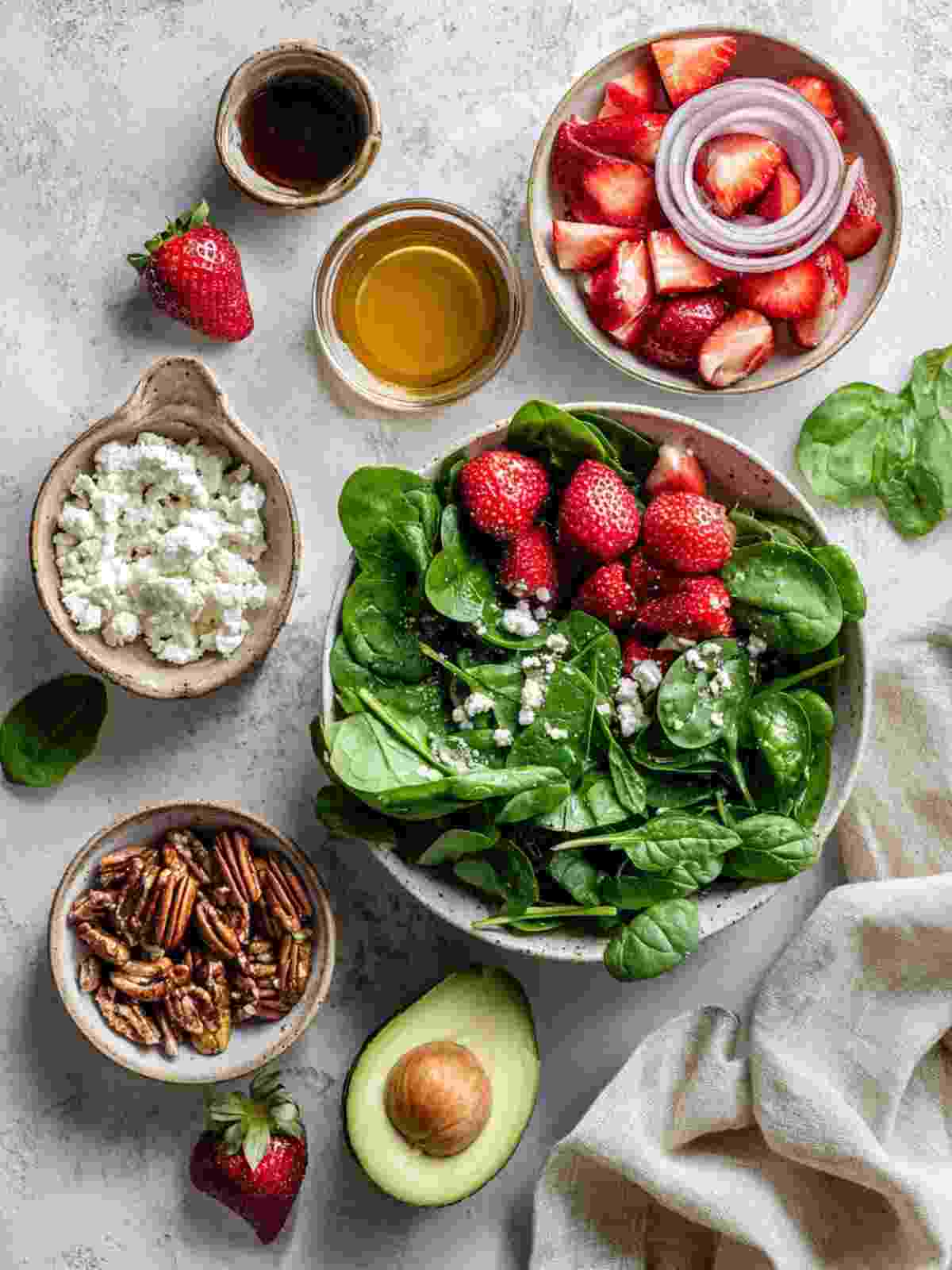 Ingredients for strawberry spinach salad including spinach, strawberries, feta, pecans, red onion, and balsamic dressing items